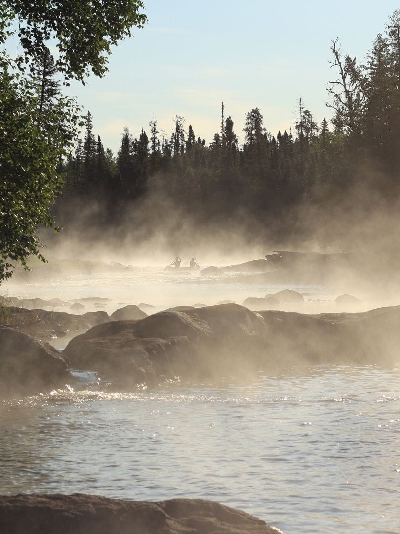 Canot double d'Expé Boréale sur une rivière dans la brume avant un rapide